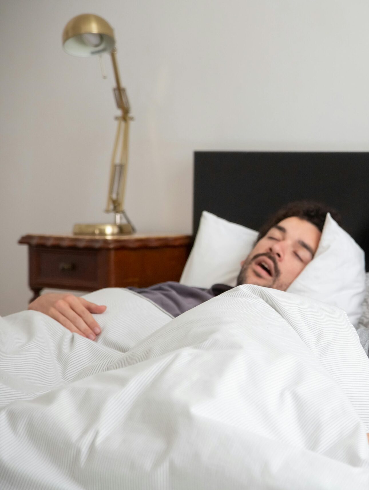 A couple in bed, with one partner covering their face due to the other's snoring.